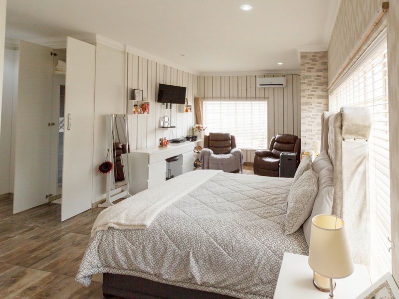 Spacious bedroom featuring wood-look flooring, built-in wardrobe, air conditioning, and modern wall paneling with ample natural light through venetian blinds.