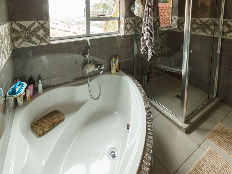 A functional bathroom featuring a built-in corner bathtub, a separate glass-enclosed shower, and decorative tiled wall accents.