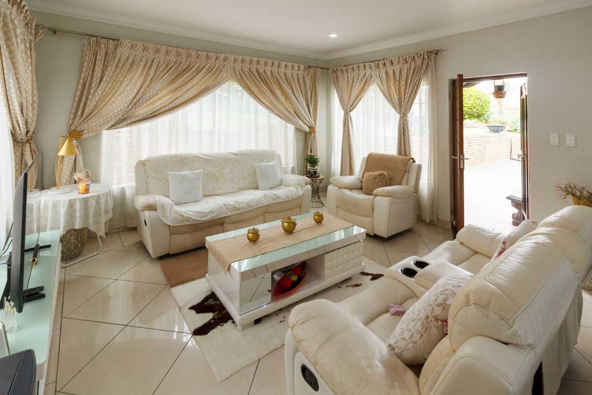 A bright and spacious living room featuring large windows with curtains, tiled flooring, and direct access to an outdoor patio area.