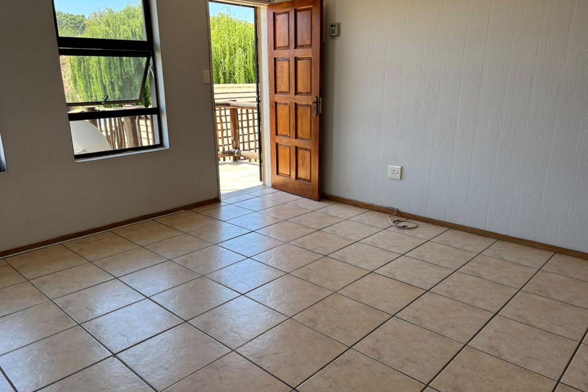 An empty living room featuring neutral tiled flooring, a timber door leading to an outdoor area, and large windows providing natural light.