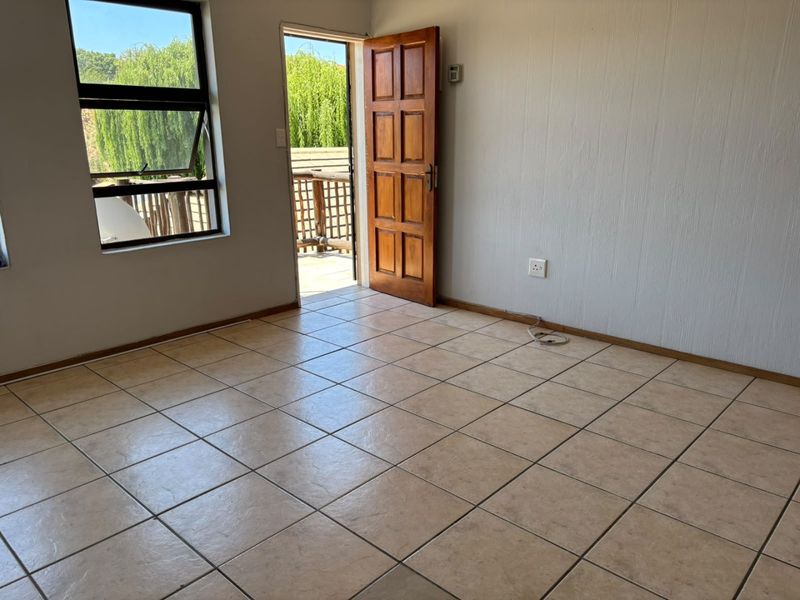 An empty living room featuring neutral tiled flooring, a timber door leading to an outdoor area, and large windows providing natural light.