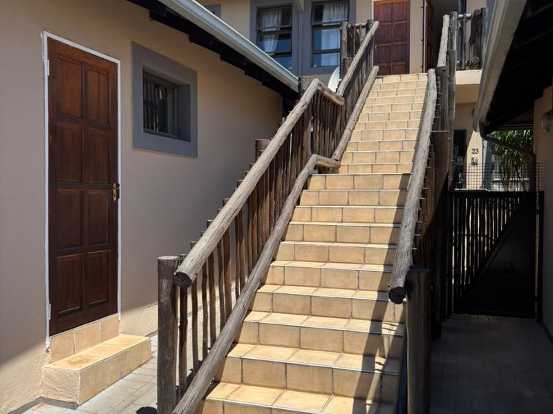 Exterior view of an apartment complex entrance featuring a tiled staircase with wooden balustrades leading to upper-level units.