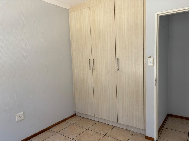 A bedroom featuring light wood-finish built-in cupboards, tiled flooring, and neutral wall paint, offering a clean and functional space.