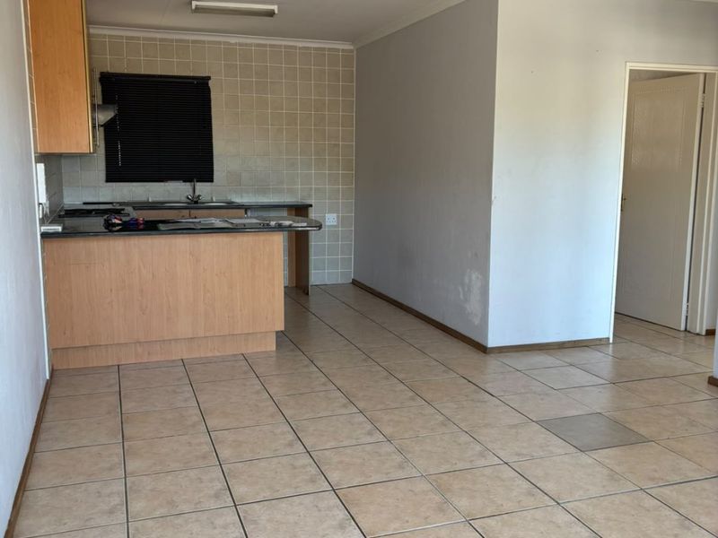 An open-plan living and kitchen area featuring tiled flooring, built-in cabinetry, and a breakfast counter, offering a blank canvas for renovation.