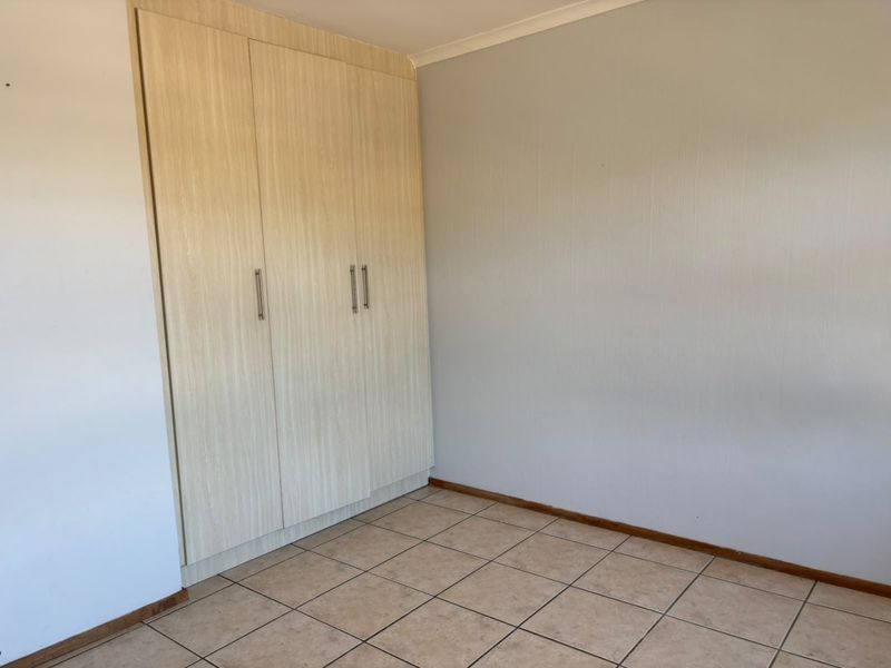 A clean, empty bedroom featuring neutral tiled flooring and a functional built-in wardrobe with light wood-grain finish doors.