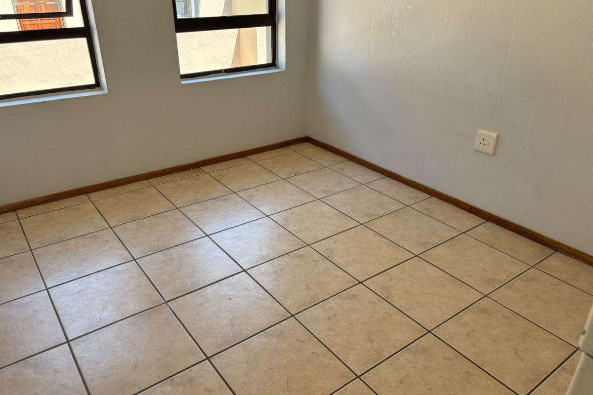 An empty bedroom featuring neutral ceramic floor tiles, white walls, and aluminium-framed windows, providing a blank canvas for interior design.
