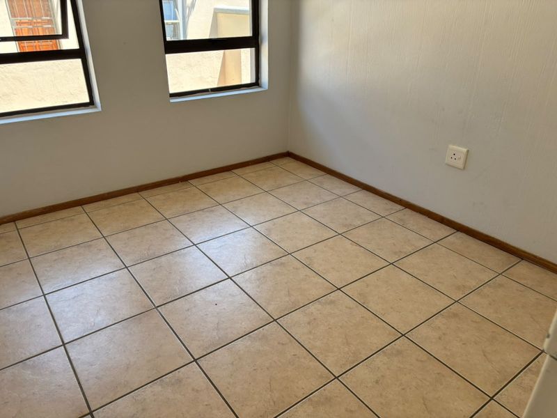 An empty bedroom featuring neutral ceramic floor tiles, white walls, and aluminium-framed windows, providing a blank canvas for interior design.