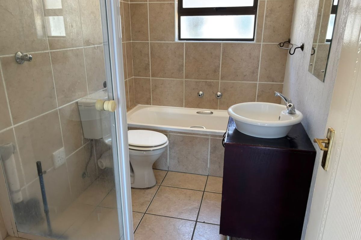 A functional bathroom featuring a built-in bathtub, separate shower enclosure, toilet, and a vanity basin with tiled finishes throughout.