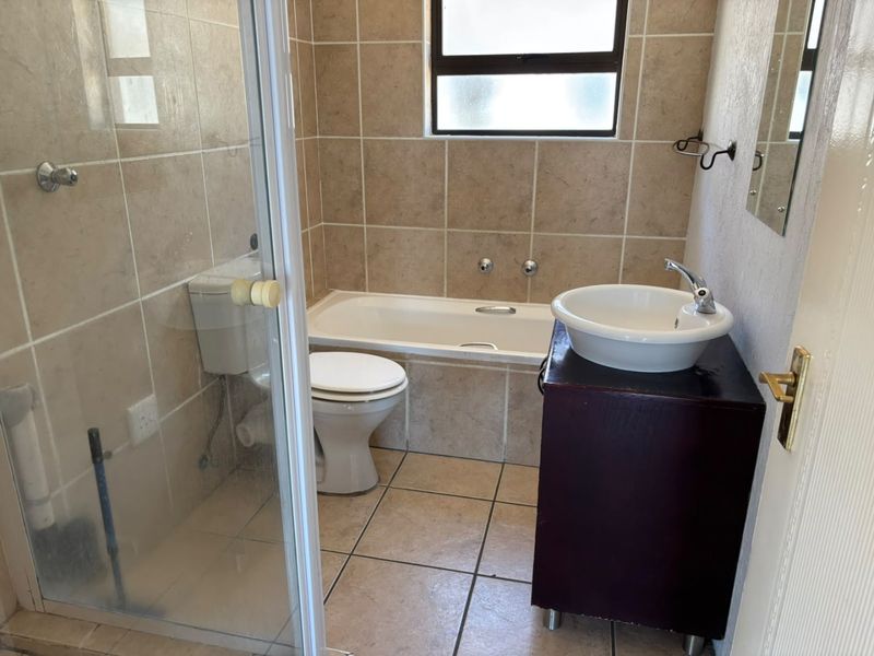A functional bathroom featuring a built-in bathtub, separate shower enclosure, toilet, and a vanity basin with tiled finishes throughout.