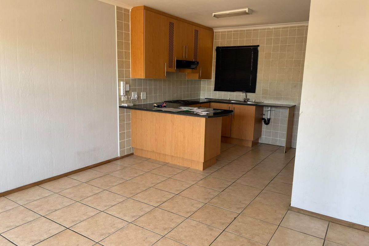 A functional kitchen area featuring tiled flooring, built-in wooden cabinetry, and a tiled backsplash, currently awaiting updates to fixtures and finishes.