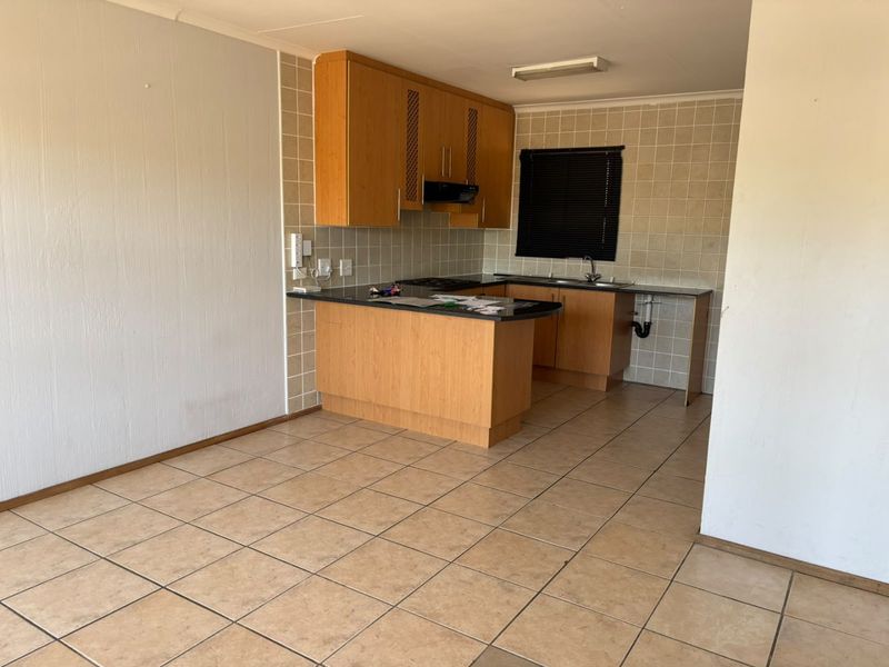 A functional kitchen area featuring tiled flooring, built-in wooden cabinetry, and a tiled backsplash, currently awaiting updates to fixtures and finishes.