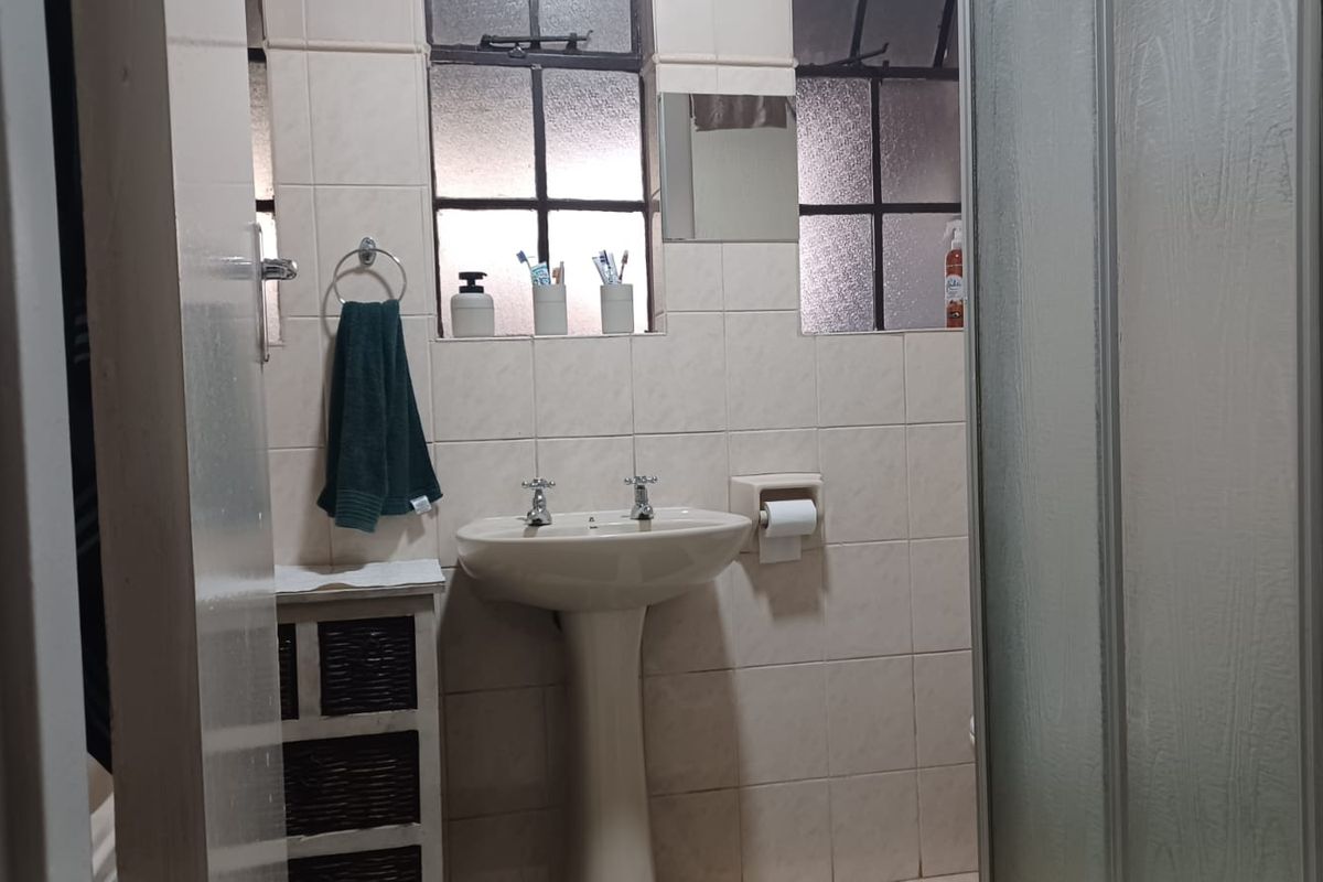 A functional bathroom featuring a pedestal basin, tiled walls, and a shower enclosure with a glass door.