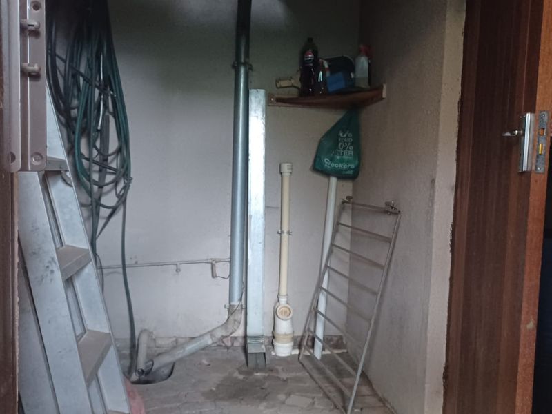 A small, unfinished utility space featuring exposed plumbing and drainage pipes, suitable for storage or conversion into a functional laundry or utility area.