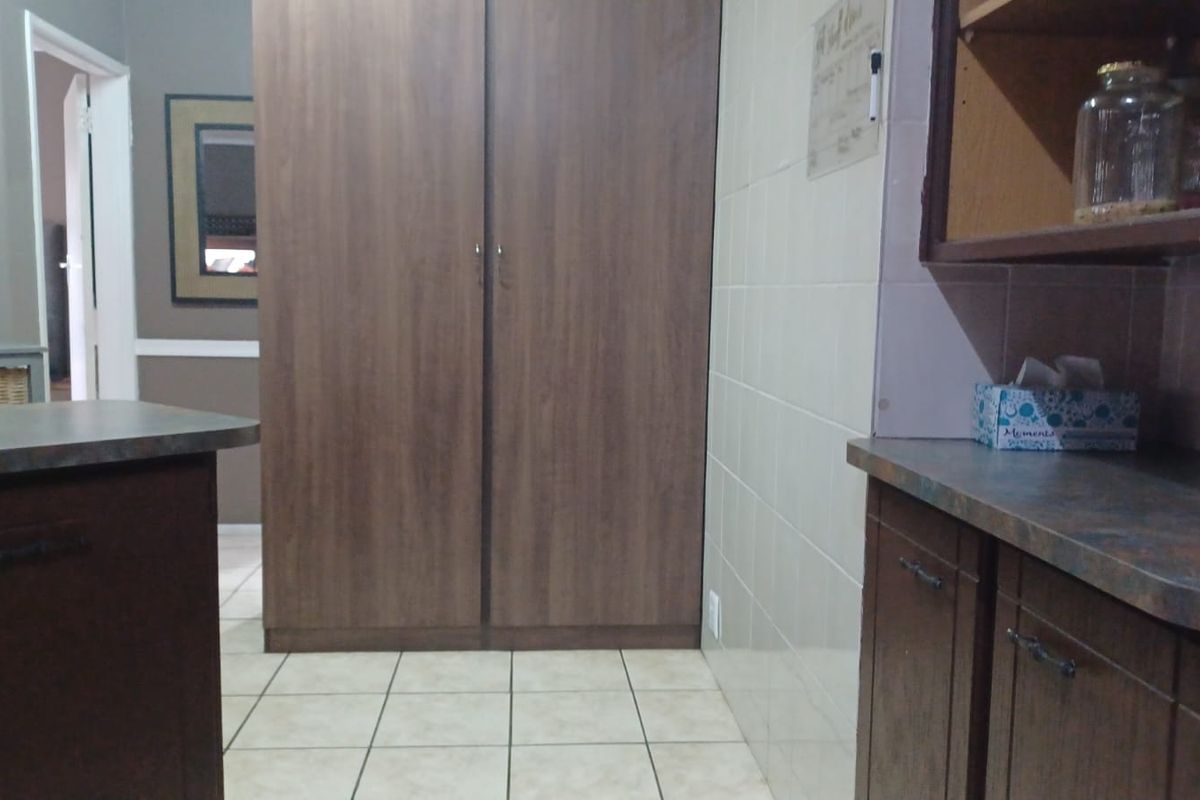 A functional kitchen area featuring built-in wood-finish cabinetry, laminate countertops, and tiled flooring with a neutral wall splashback.
