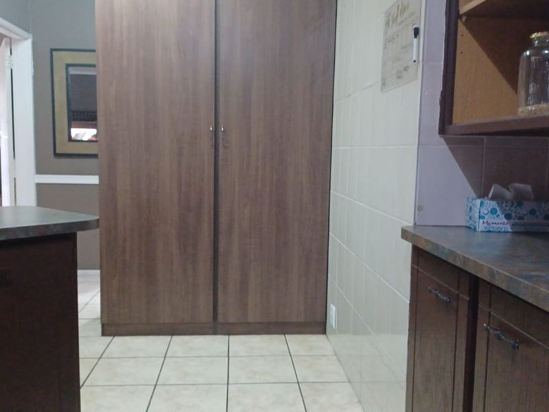 A functional kitchen area featuring built-in wood-finish cabinetry, laminate countertops, and tiled flooring with a neutral wall splashback.