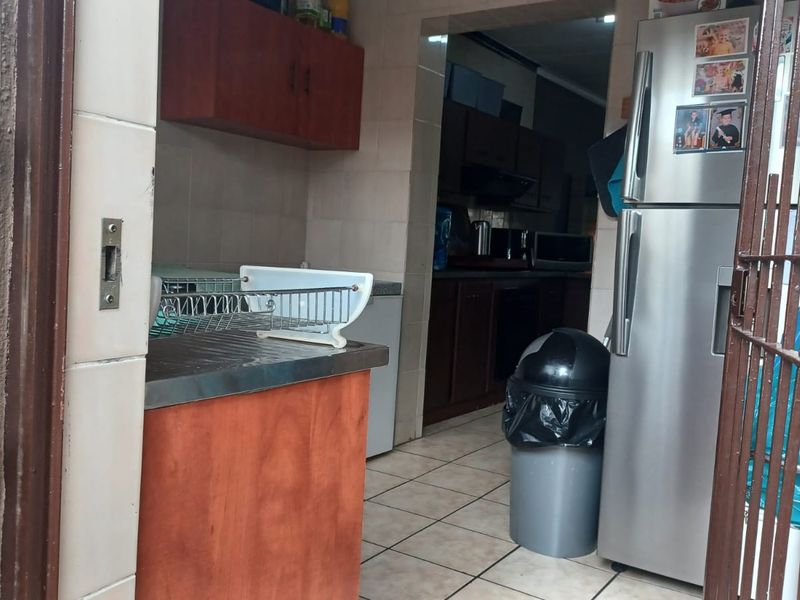 A functional scullery area featuring built-in cabinetry, tiled flooring, and a stainless steel countertop, providing additional workspace and storage adjacent to the main kitchen.