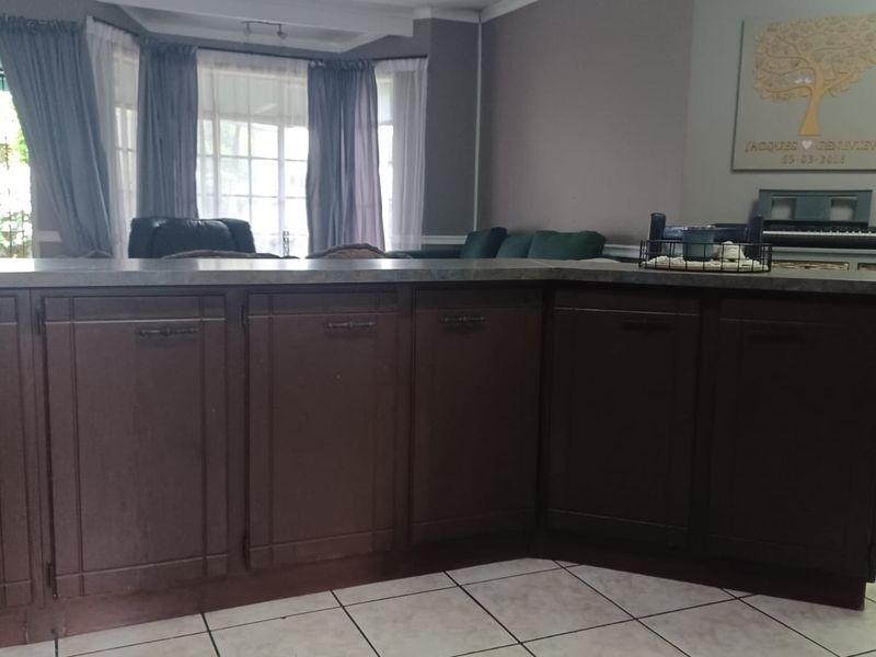 Open plan living area featuring a kitchen island with dark cabinetry, laminate countertops, and ceramic floor tiles, leading into a bright lounge with bay windows.