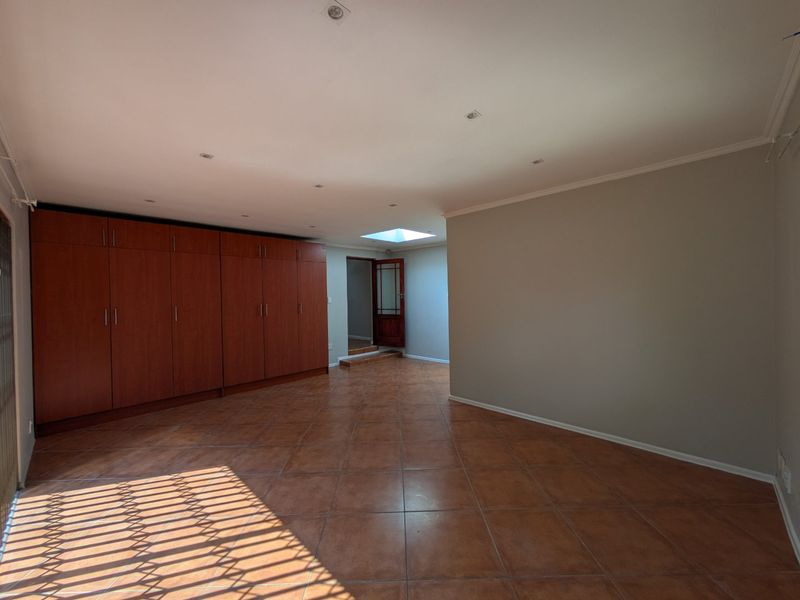 Spacious bedroom featuring extensive built-in cupboards, tiled flooring, and a skylight, providing a bright and functional living space.