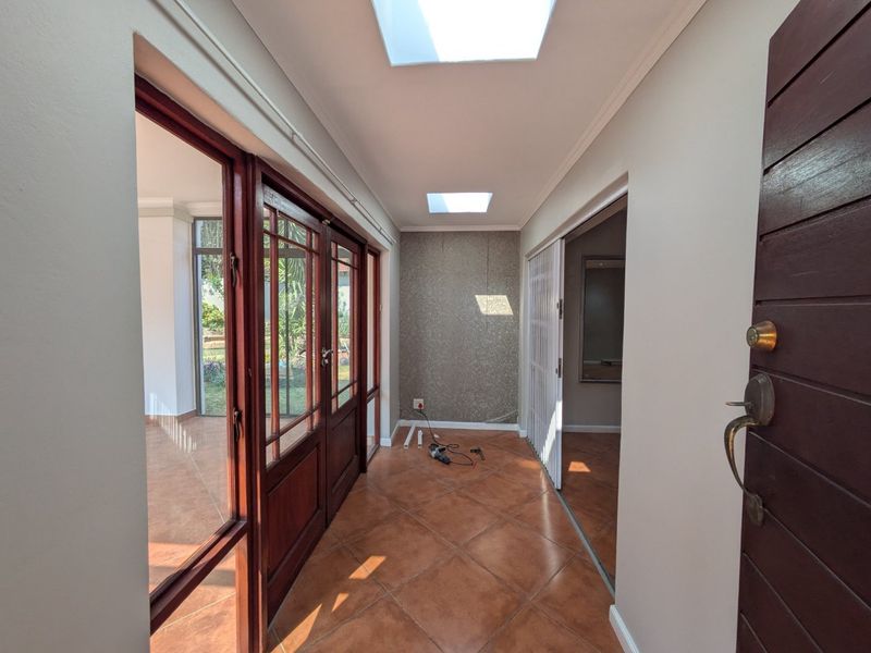 Bright entrance hall featuring tiled flooring, dual skylights, and timber-framed glass doors leading to the living area.