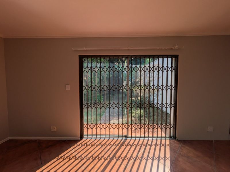 An empty living room featuring tiled flooring and a sliding glass door with a security gate, providing direct access to the outdoor area.
