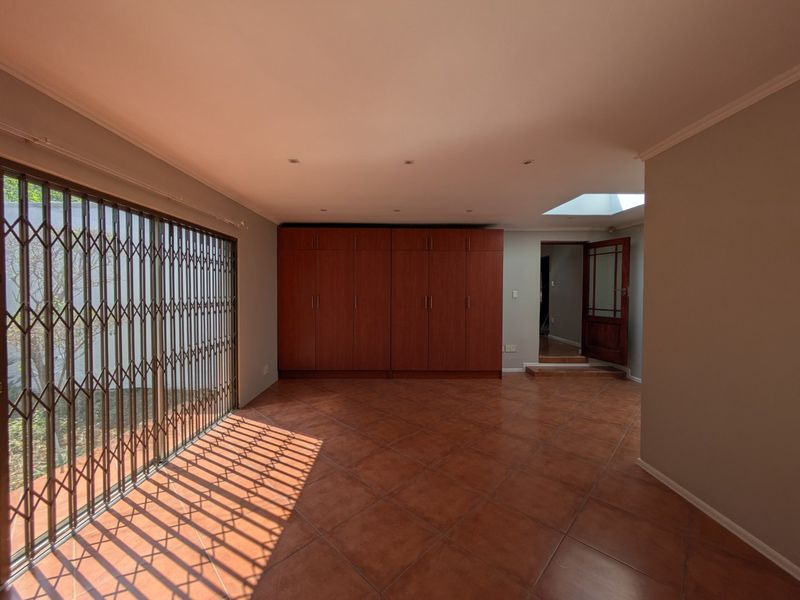 Spacious living area featuring tiled flooring, built-in storage cupboards, recessed lighting, a skylight, and a sliding door with security gate access to the exterior.