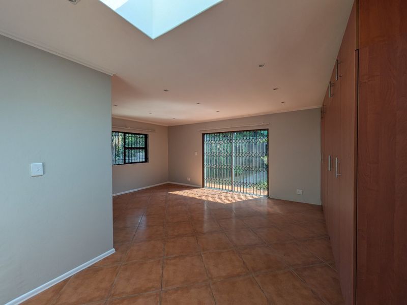 Spacious living area featuring tiled flooring, built-in cupboards, a large skylight for natural light, and sliding doors leading to the exterior.
