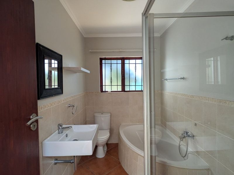 A functional bathroom featuring a wall-mounted basin, toilet, built-in bathtub, and a separate shower enclosure with tiled finishes throughout.