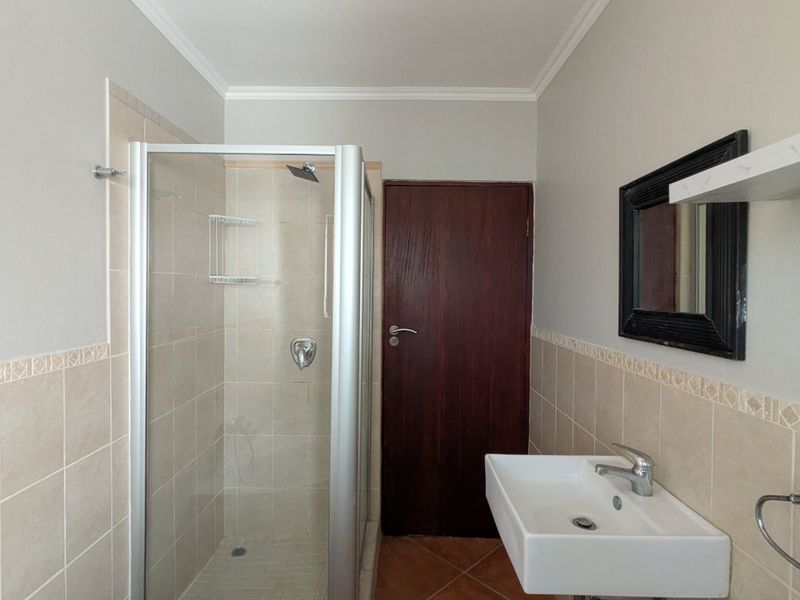 A functional bathroom featuring a shower enclosure, wall-mounted basin, and tiled finishes throughout.