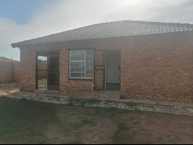 Rear view of a face brick house featuring a tiled roof, security gates on doors and windows, and a paved walkway leading to the garden.