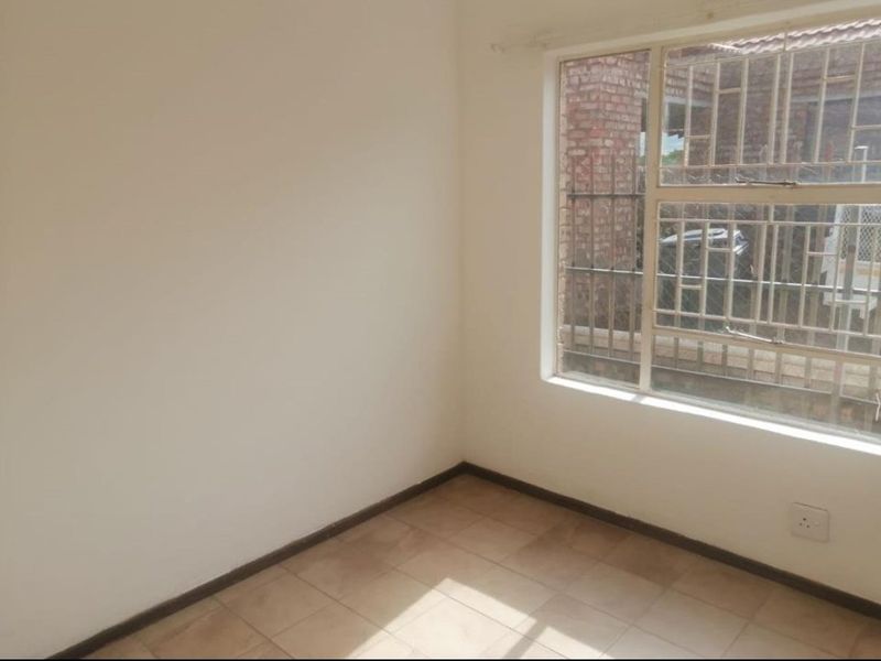 A simple, empty bedroom featuring tiled flooring and a window fitted with security bars, offering a blank canvas for personalization.