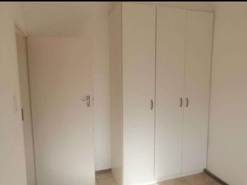 A simple bedroom interior featuring neutral white walls, tiled flooring, and built-in cupboards.