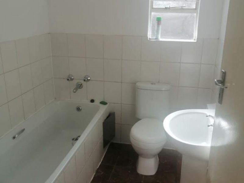 A functional bathroom featuring a bathtub, pedestal basin, and toilet with tiled finishes and a window with security bars.