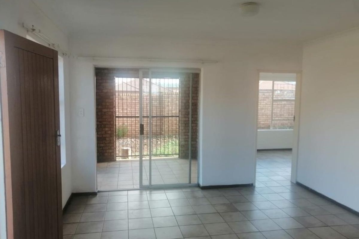 An empty living area featuring tiled flooring and a sliding glass door providing access to an outdoor patio space.