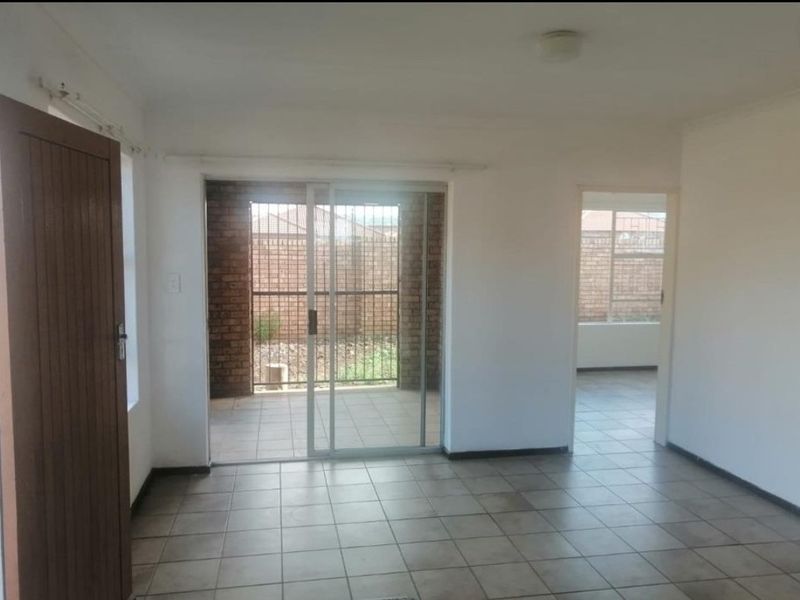 An empty living area featuring tiled flooring and a sliding glass door providing access to an outdoor patio space.