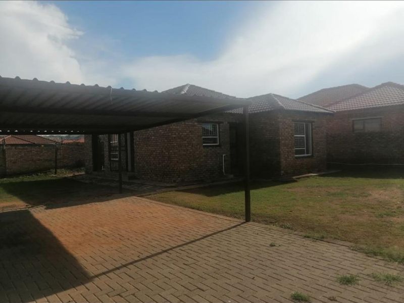 Front exterior view of a face brick house featuring a paved driveway, attached carport, and tiled roof with security bars on windows.