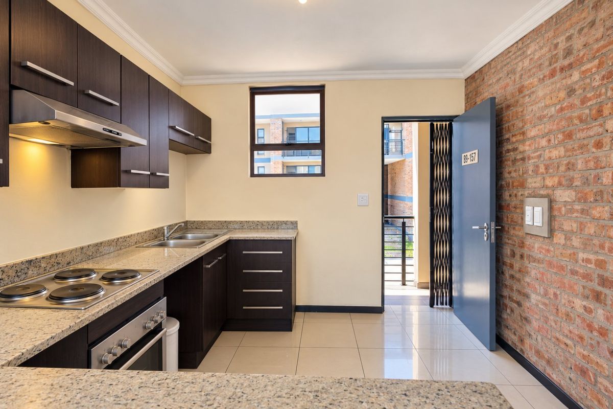Modern kitchen featuring dark wood cabinetry, granite countertops, integrated appliances, and an exposed brick feature wall, leading to an exterior entrance.