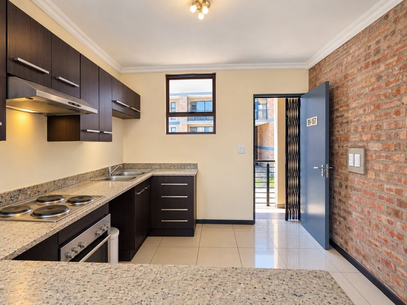Modern kitchen featuring dark wood cabinetry, granite countertops, integrated appliances, and an exposed brick feature wall, leading to an exterior entrance.