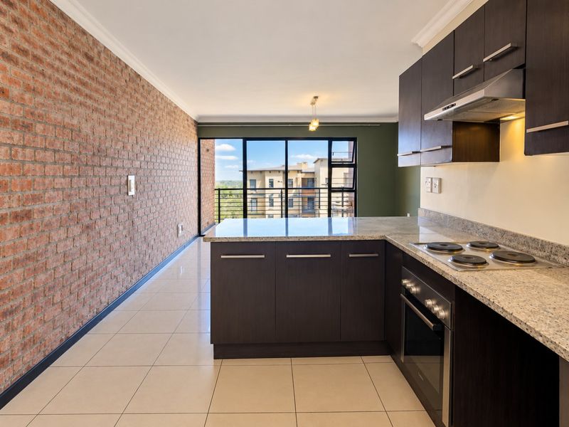 Modern open-plan kitchen and living area featuring an exposed brick feature wall, granite countertops, built-in appliances, and access to a balcony with views.