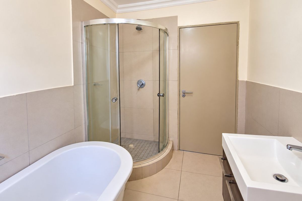 Modern bathroom featuring a freestanding bathtub, a curved glass shower enclosure, and a sleek vanity basin with neutral tiled finishes.