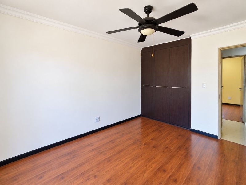A clean, empty bedroom featuring dark wood-look laminate flooring, a ceiling fan, and built-in dark wood cupboards with modern hardware.