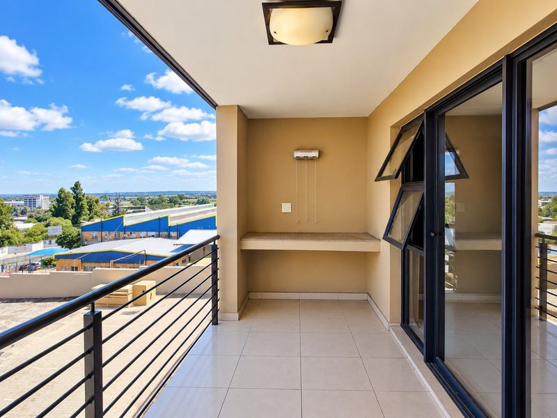 A spacious covered balcony featuring tiled flooring, a built-in stone counter, and a metal balustrade, offering an open view of the surrounding area.