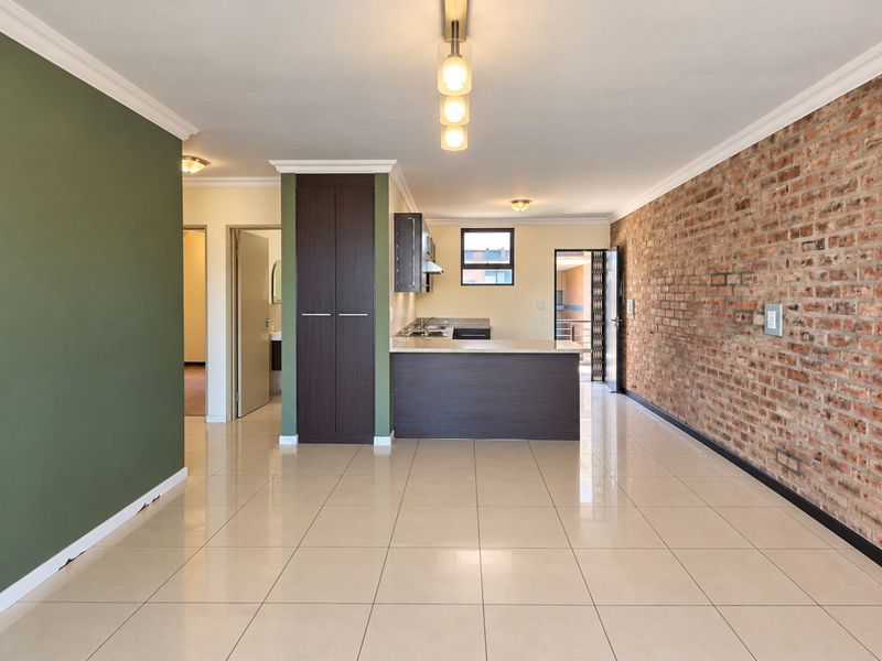 Spacious open-plan living area featuring polished tile floors, a striking exposed brick feature wall, and a functional kitchen with stone countertops.