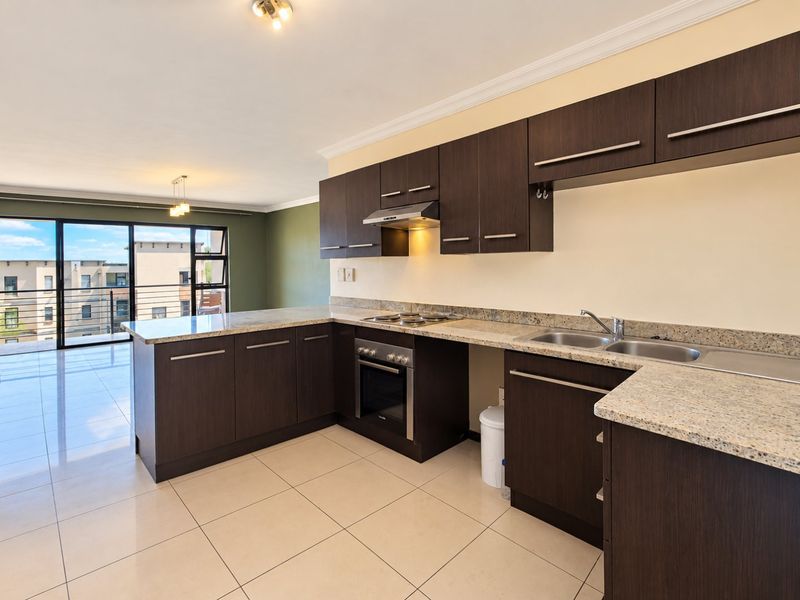 Open-plan kitchen featuring dark wood cabinetry, granite countertops, and built-in appliances, flowing into a bright living area with access to a balcony.