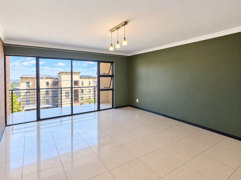 Spacious, empty living area featuring large sliding glass doors leading to a balcony, tiled flooring, and a modern ceiling light fixture.