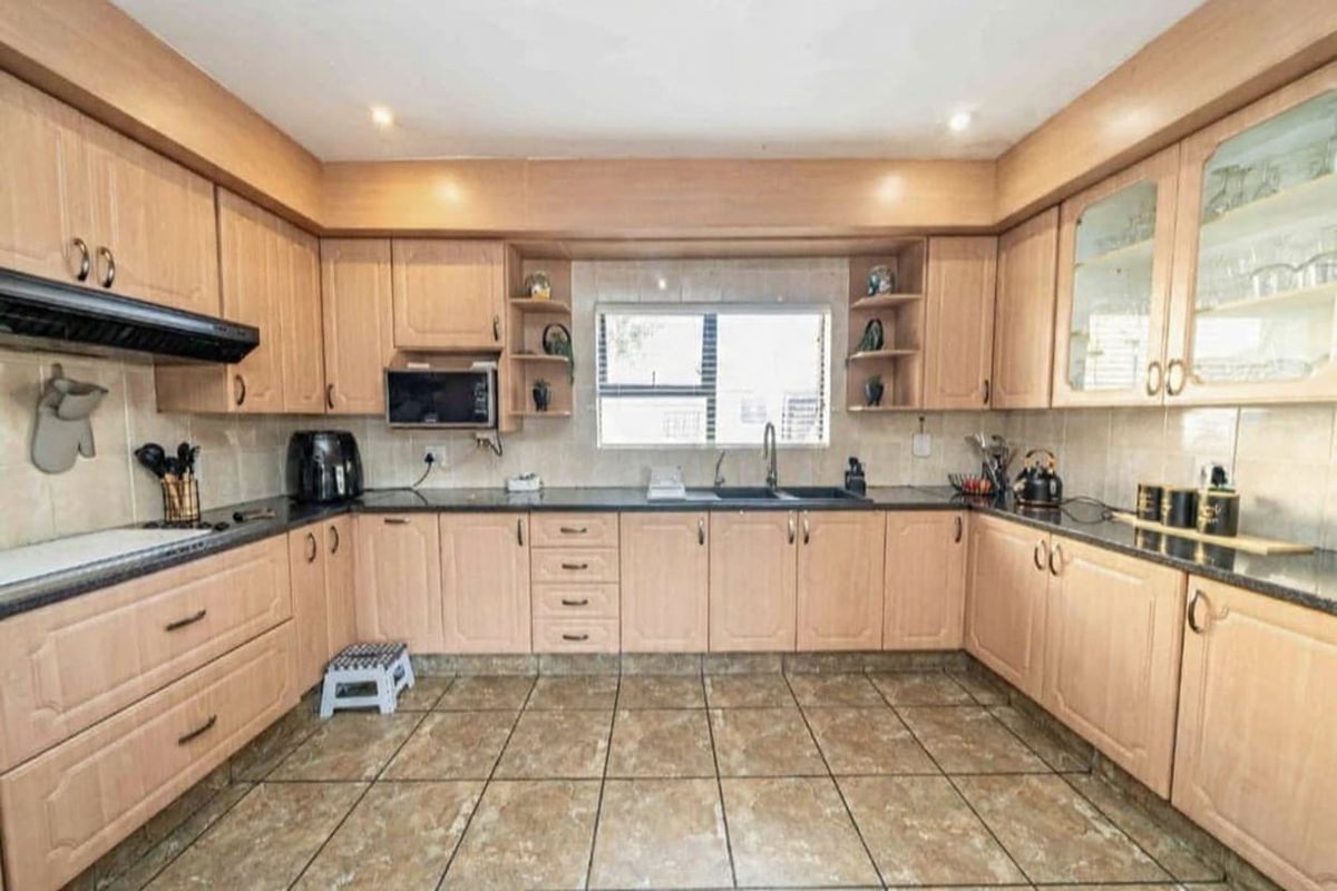 A functional U-shaped kitchen featuring light wood cabinetry, dark laminate countertops, tiled flooring, and a built-in extractor fan.