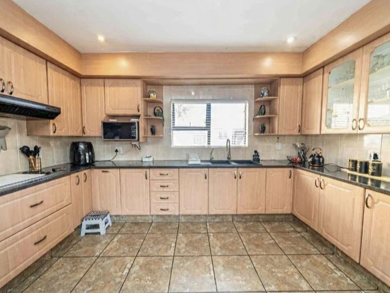 A functional U-shaped kitchen featuring light wood cabinetry, dark laminate countertops, tiled flooring, and a built-in extractor fan.
