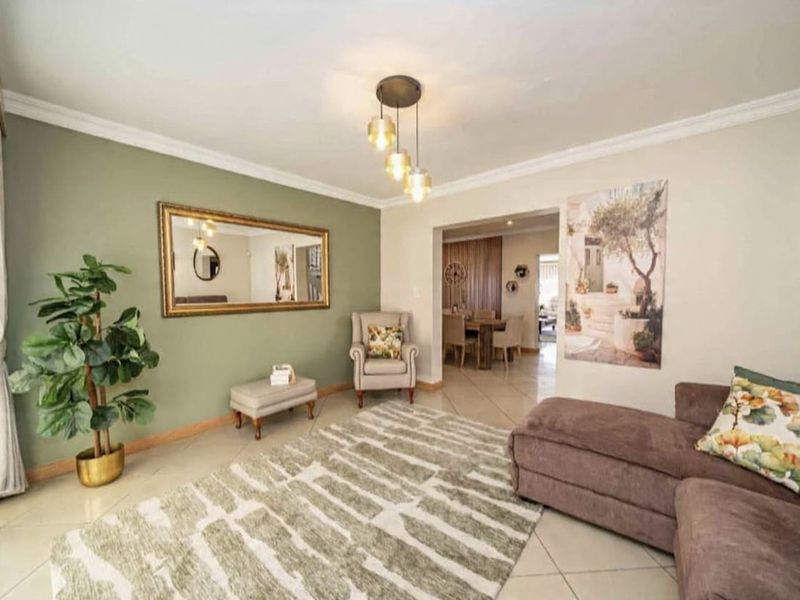 A well-maintained living room featuring neutral tiled flooring, elegant crown molding, and a modern pendant light fixture, leading into an adjacent dining area.