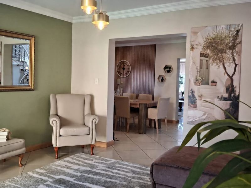 An open-plan living and dining area featuring tiled floors, crown molding, and a modern slatted wood accent wall in the dining space.