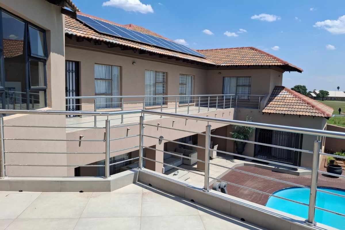 Rear elevation featuring a spacious tiled balcony with stainless steel balustrades, overlooking a swimming pool and garden area with roof-mounted solar panels.