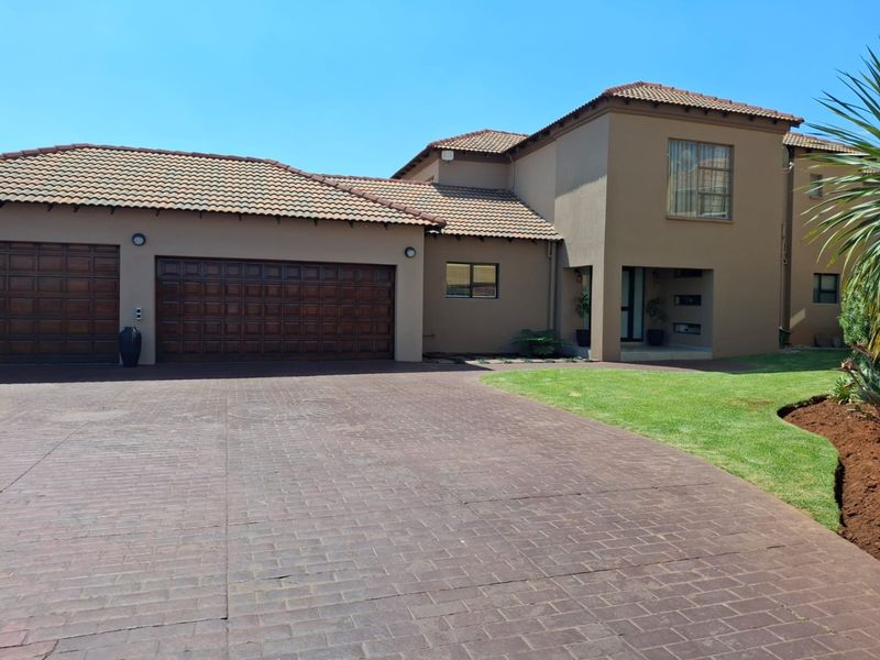 A well-maintained double-story house featuring a paved driveway, double garage, and neat front garden with a covered entrance.